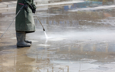 A man in a green coat is standing in the rain, holding a pressure washer