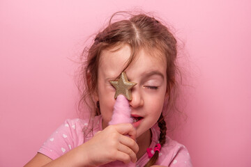 Close up portrait of cheerful young girl with braided hair holding golden star decoration against...