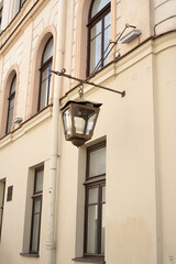 weathered bronze street lantern suspended from ornate wrought bracket on tranquil cream-beige...