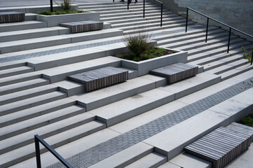 multi-tiered concrete stair plaza in modern urban courtyard featuring integrated wooden slat benches, geometric planter boxes with grasses, black metal railings, repeating gray lines and minimalist, c