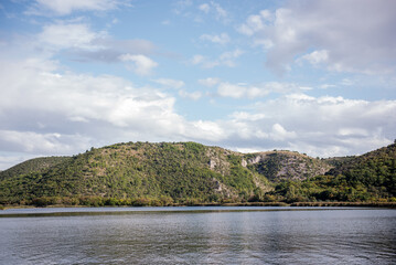 Visovac lake reflecting the cloudy sky with its calm waters surrounded by lush vegetation and hills, a beautiful landscape in Krka national park, Croatia, during a sunny day