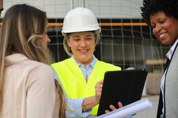 Team of architects and engineers discussing building project using digital tablet and blueprints on...