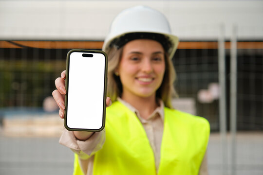 Architect showing smartphone with blank white screen in front of construction site