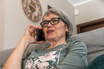 Senior woman's hand holding smartphone to ear, casual conversation in home setting, Poland