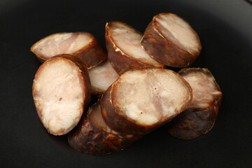 Sliced smoked sausage arranged on a black plate showcasing rich colors and textures