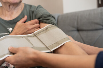 Close-up of senior woman preparing for blood pressure measurement, adjusting sleeve with cuff on arm, concept of home healthcare