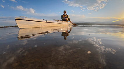 low angle view of a senior canoe paddler on a calm lake at sunset