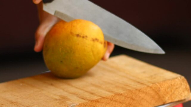 Hand slicing perfectly ripe mango - Juicy mango slice cut and showcased on wooden board, the slice is shown resting with natural movement. Mango, 