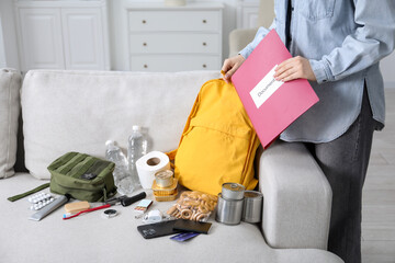 Survival kit. Woman putting documents into backpack indoors, closeup