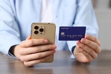 Woman with credit card and smartphone paying online at wooden table, closeup