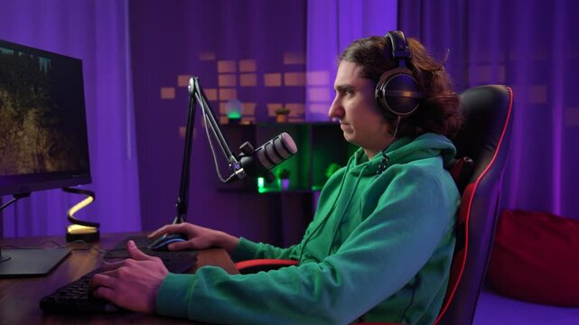 Young adult man spending time at home, man streamer gamer sits at desk with computer in neon lighted room streaming online and losing game, frustrated expression.