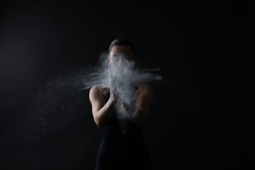 Woman clapping hands with talcum powder before training on black background