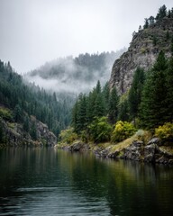 A misty river winds through a forested mountain valley with rocky cliffs and lush green trees.