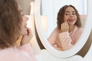 Happy woman plucking her mustache with tweezers near mirror at home