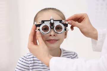Ophthalmologist examining girl's vision with trial frame in clinic, closeup