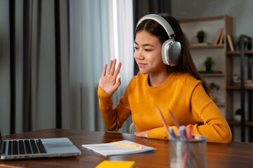 Focused student with headphones writing in notepad with laptop nearby
