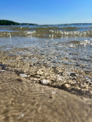 Close up of beach sand and ocean water, blue sky in background