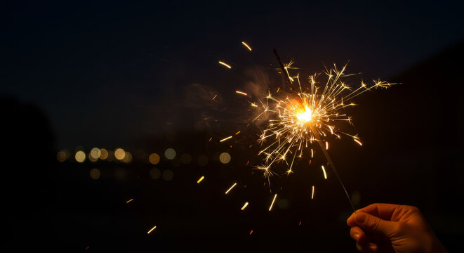 Hand holding a sparkler against a dark background.