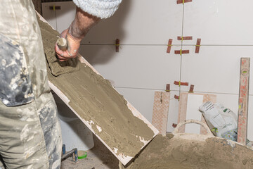 Tiler applying adhesive on ceramic tile with notched trowel, preparing it for wall installation