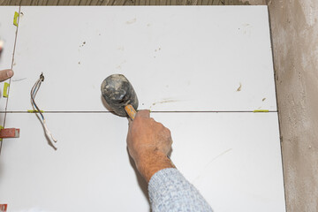 Tiler placing ceramic tiles on the wall using rubber mallet and levelers