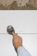 Tiler placing ceramic tiles on a wall using a rubber mallet and tile spacers during renovation work