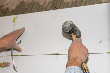 Tiler placing large format tile on wall using rubber mallet and leveling system during renovation works