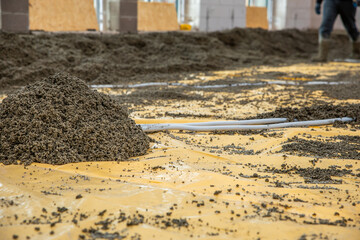 A construction site featuring a gravel pile on a yellow plastic sheet, pipes arranged for...