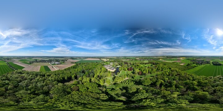 Aerial 360&deg; panorama of Schloss Dyck near Grevenbroich, Germany: historic castle, blooming gardens, orchards, and lush countryside in full spring bloom under a vibrant blue sky.