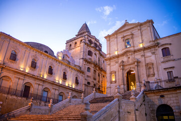 Fototapeta premium Staircase of the chiesa di San Francesco d'Assisi all'Immacolata next to the rear of the chiesa di San Salvatore in Noto, Sicily, Italy, with artificial lighting at dusk