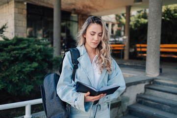 Fototapeta premium University student reading notes outdoors while holding a backpack