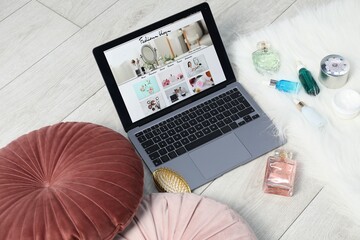 Laptop with fashion blog web site, perfumes, cosmetics and brush on floor indoors, above view