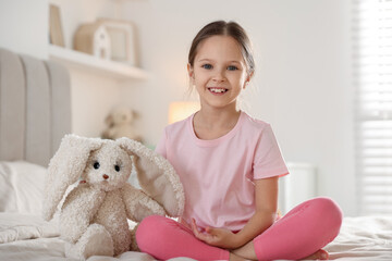 Cute girl with toy bunny on bed at home