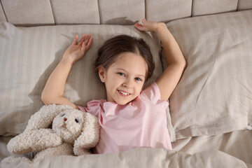 Cute girl with toy bunny in bed, above view