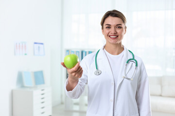 Nutritionist with green apple and stethoscope in clinic, space for text