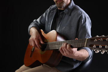 Man playing guitar on chair against black background, closeup