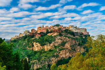 Fototapeta premium beautiful highland landscape of old town on a top of amazing mountain with green slopes and trees on foreground and amazing blue cloudy sky on background