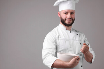 Happy confectioner in uniform holding whisk and bowl on light grey background