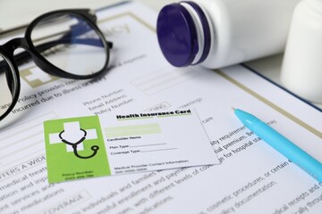 Health insurance card, policy, pen and medical bottles on white table, closeup