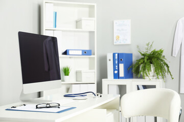 Fototapeta premium Doctor's workplace. Computer monitor, clipboard, stethoscope and glasses on white table in medical office