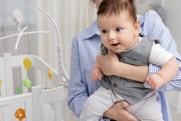 Mother holding her little baby, closeup. Crib with cot mobile in nursery