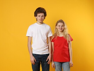 Fototapeta premium Young woman and man wearing blank t-shirts on orange background. Mockup for design