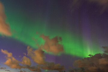 Magnificent Northern Lights illuminate the night sky above the clouds, creating a magical natural landscape with stars.