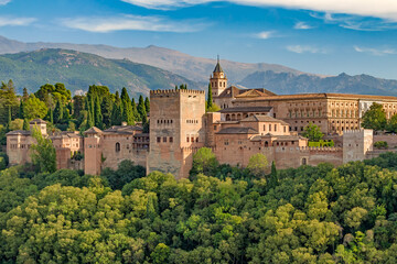 Obraz premium Panoramic view of the Alhambra fortress and palace complex in Granada, Spain, with lush forest and the Sierra Nevada mountains in the background, captured in warm golden hour light.