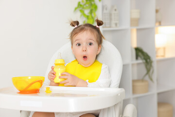 Little baby with feeding bottle of milk in high chair at home