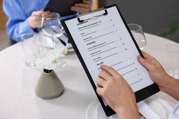 Couple choosing dishes from menu at table in restaurant, closeup