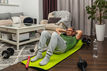 Man exercises at home using a yoga mat and weights