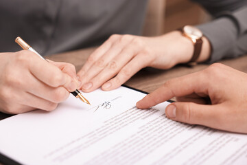 Man pointing at document and woman putting signature at table, closeup