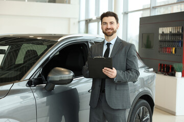 Happy salesman with clipboard near new car in salon
