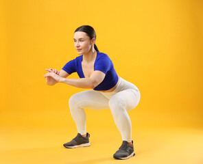 Woman in sportswear exercising on orange background