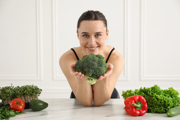 Woman in fitness clothes with broccoli at white marble table indoors. Healthy food
